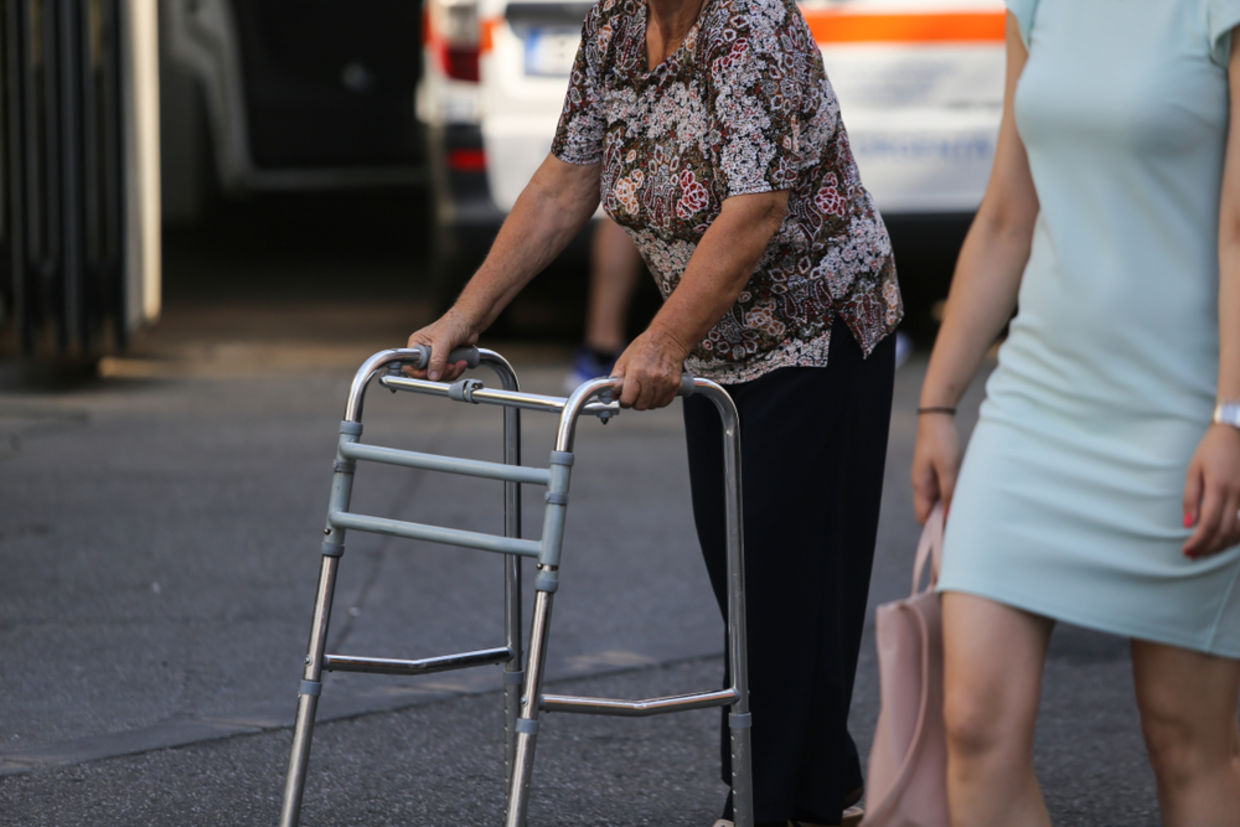 An older woman walks with the help of a walker An older woman walks with the help of a walker
