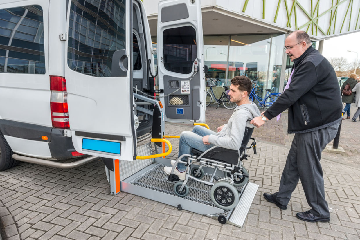 Side view of taxi driver assisting man on wheelchair to board van outside building Side view of taxi driver assisting man on wheelchair to board van outside building