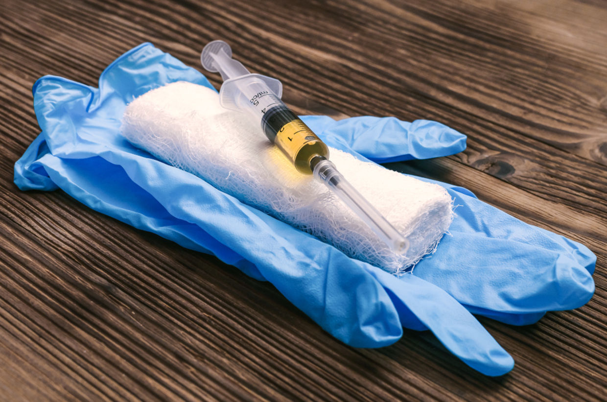 Syringe with orange drug medicine, medicinal gloves and bandage on the doctor table background Syringe with orange drug medicine, medicinal gloves and bandage on the doctor table background