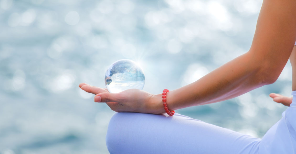 A woman meditates while holding a crystal sphere in her palm. A woman meditates while holding a crystal sphere in her palm.