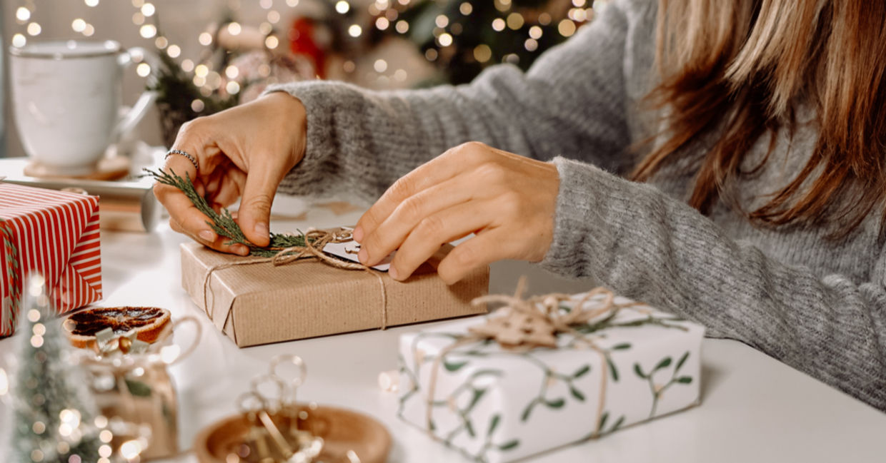 A woman sits in front of a Christmas and decorates her gifts with a sprig of juniper and DIY twine bows. A woman sits in front of a Christmas and decorates her gifts with a sprig of juniper and DIY twine bows.