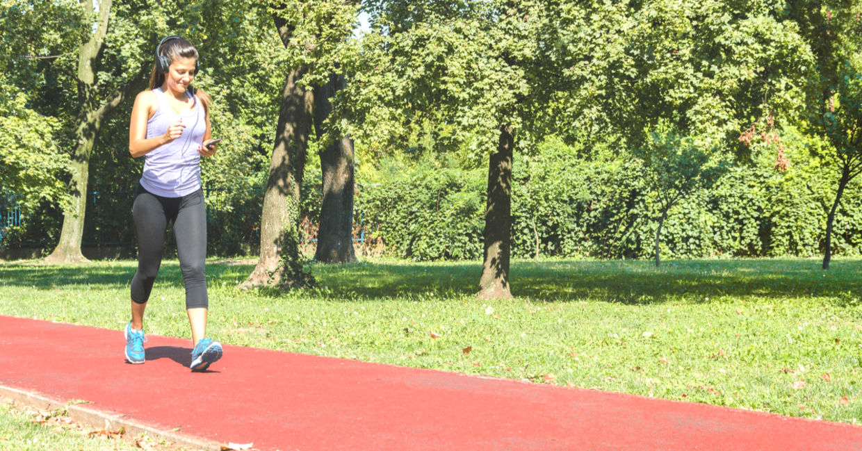 Woman walking briskly on a track listening to music. Woman walking briskly on a track listening to music.