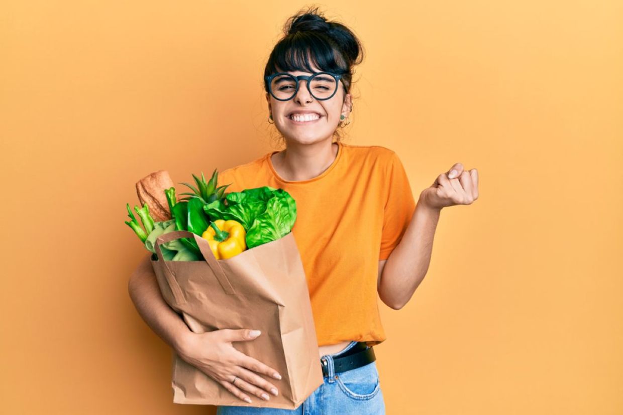 A woman smiles and holds a bag filled with food. A woman smiles and holds a bag filled with food.