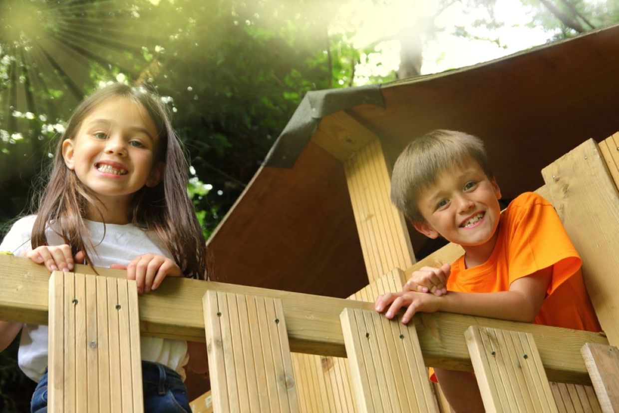 Smiling children look out from a wooden treehouse. Smiling children look out from a wooden treehouse.