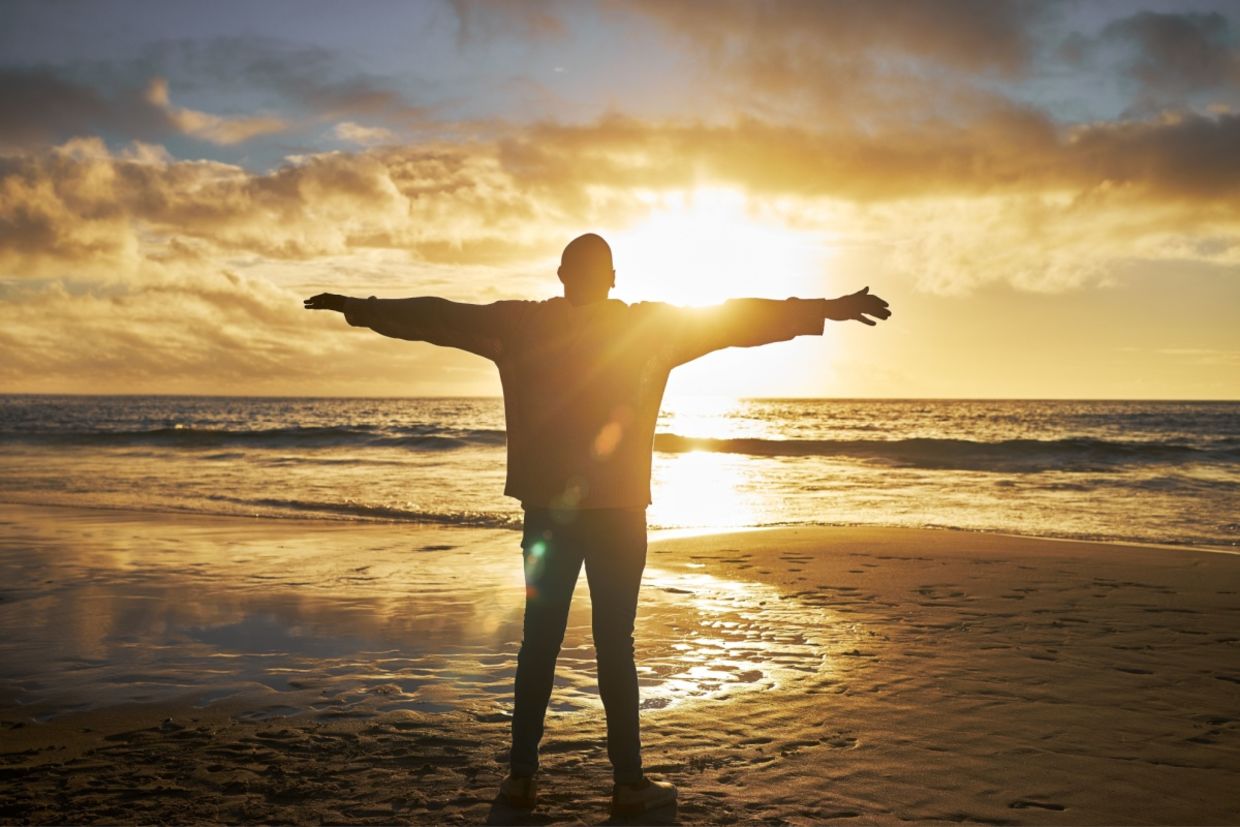 A silhouette of a man at the beach standing with his arms raised. A silhouette of a man at the beach standing with his arms raised.