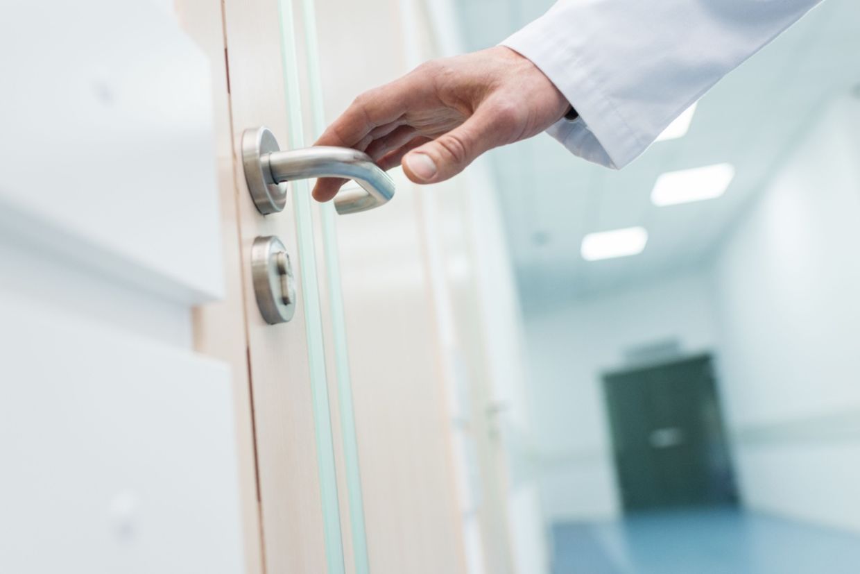 A doctor reaches for a door handle. A doctor reaches for a door handle.
