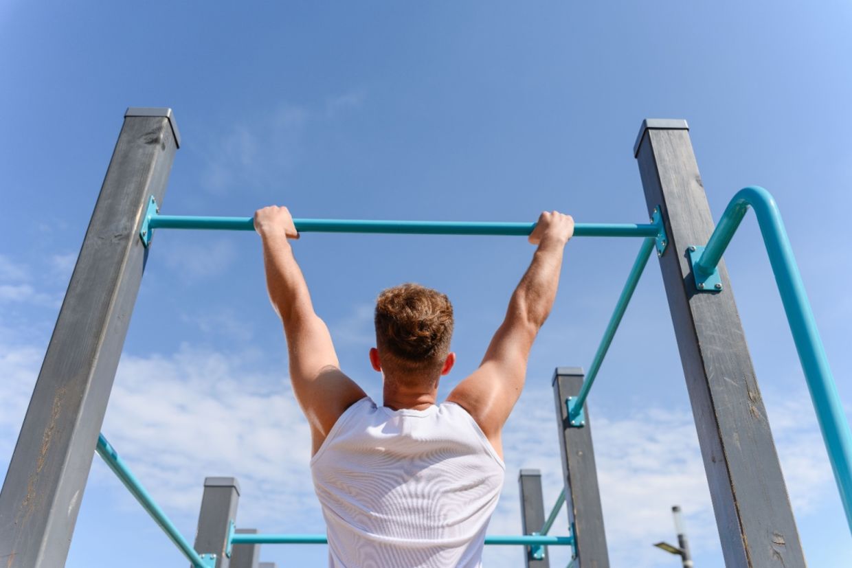 A man hangs from a bar. A man hangs from a bar.